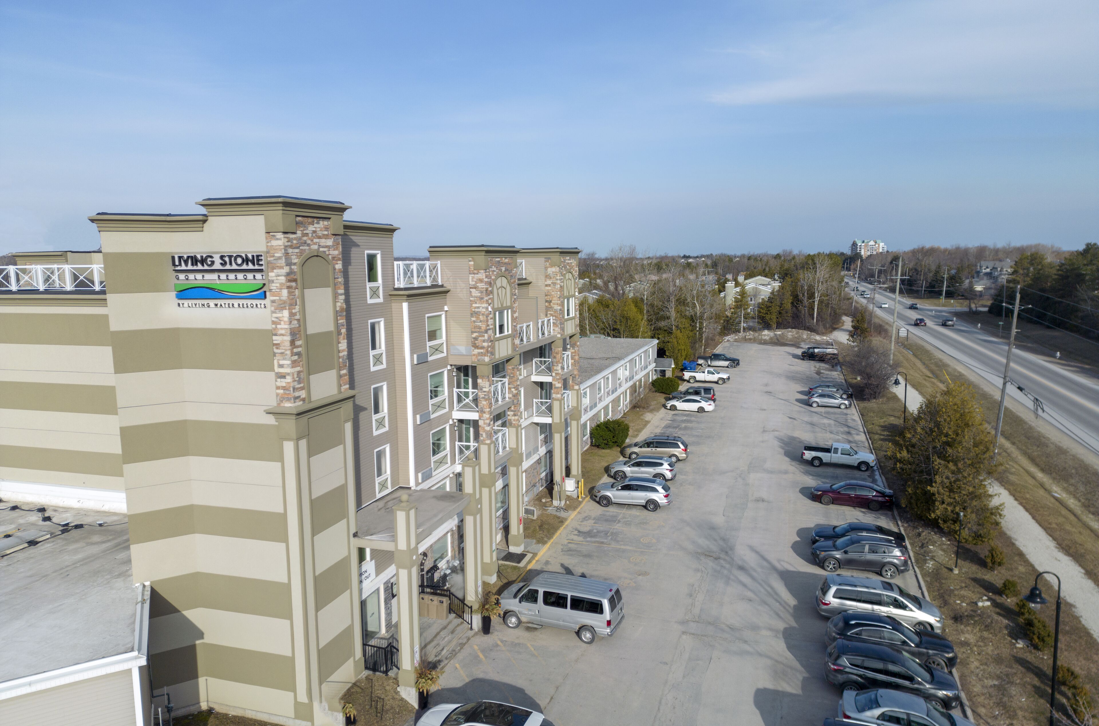 A multi-story building with a sign for 'Living Stone Golf Resort' and a parking lot with several cars.