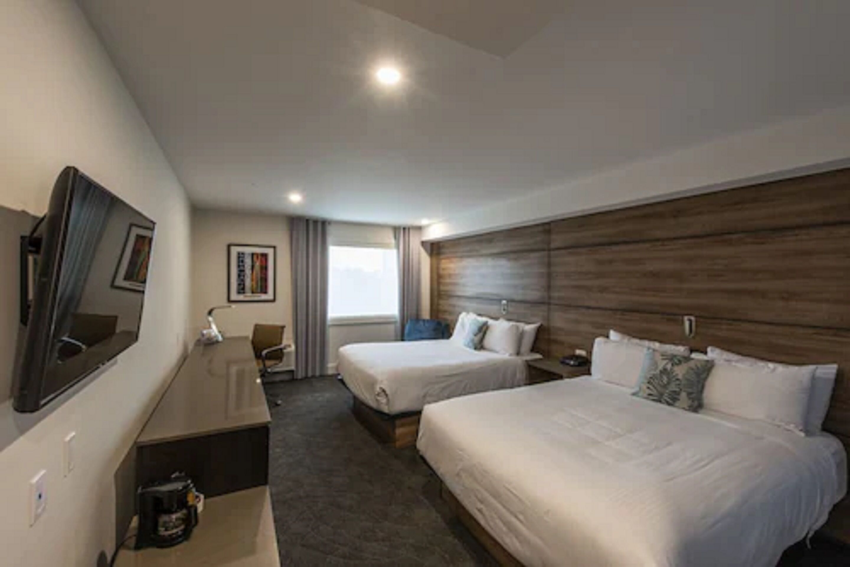 A hotel room with two beds, a desk, a chair, a TV, and a window with curtains.