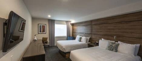 Habitación de hotel con dos camas, un escritorio, una silla, un televisor y una ventana con cortinas.