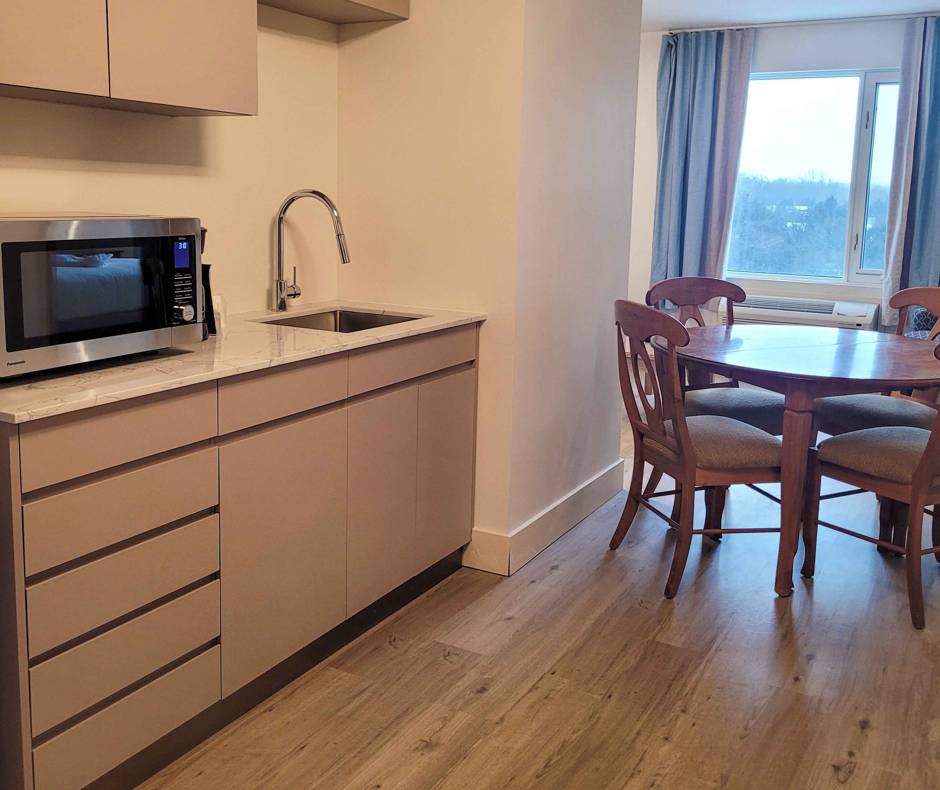 A compact kitchen with a microwave, sink, and wooden dining table with chairs.