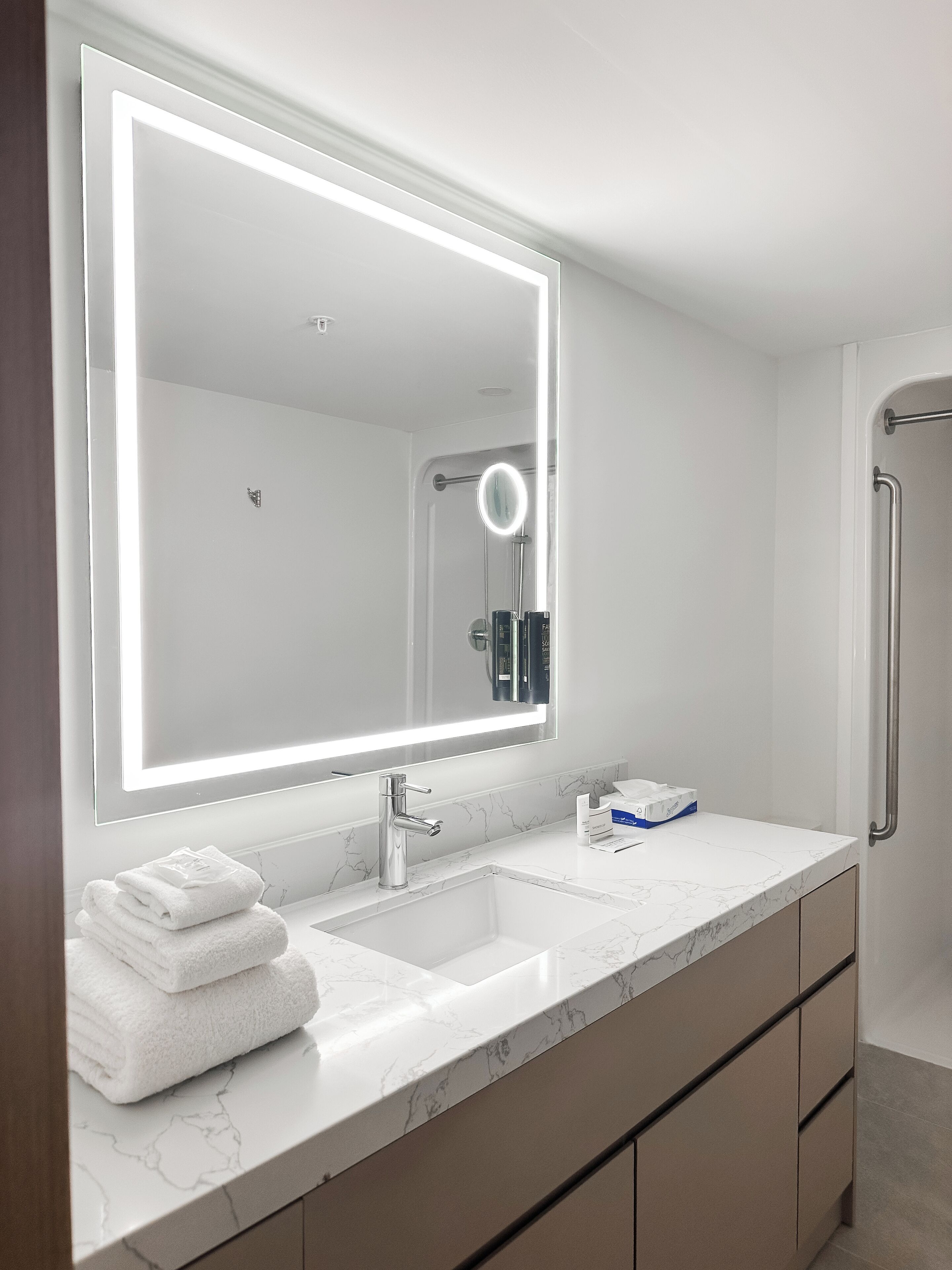 A modern bathroom with a large mirror, white marble countertop, and a towel stack.