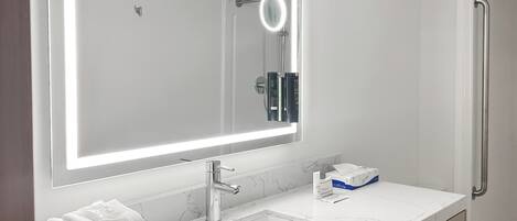 A modern bathroom with a large mirror, white marble countertop, and a towel stack.
