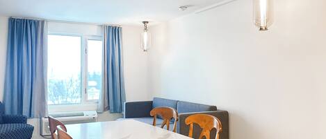 Un comedor con una mesa blanca, sillas de madera, un sofá azul y dos lámparas colgantes.