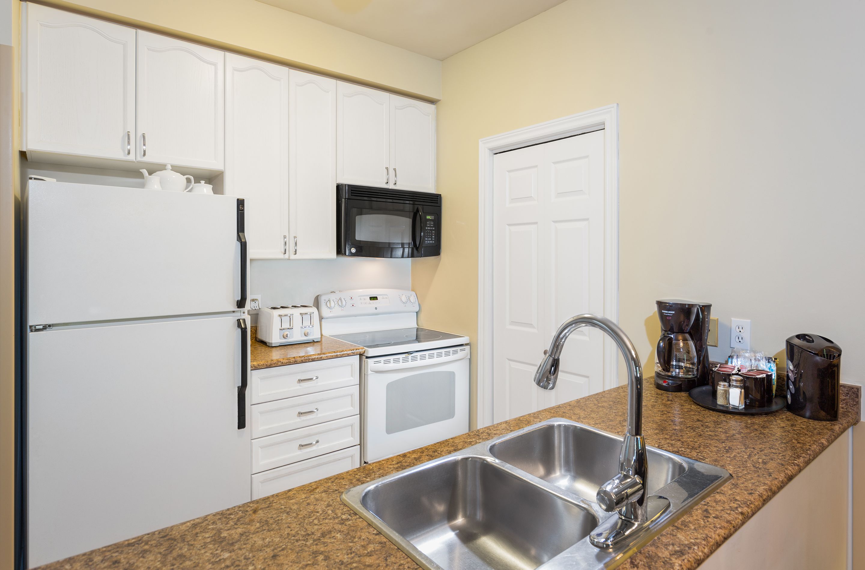 A kitchen with white cabinets, a stainless steel sink, a microwave, a toaster, and a coffee maker.