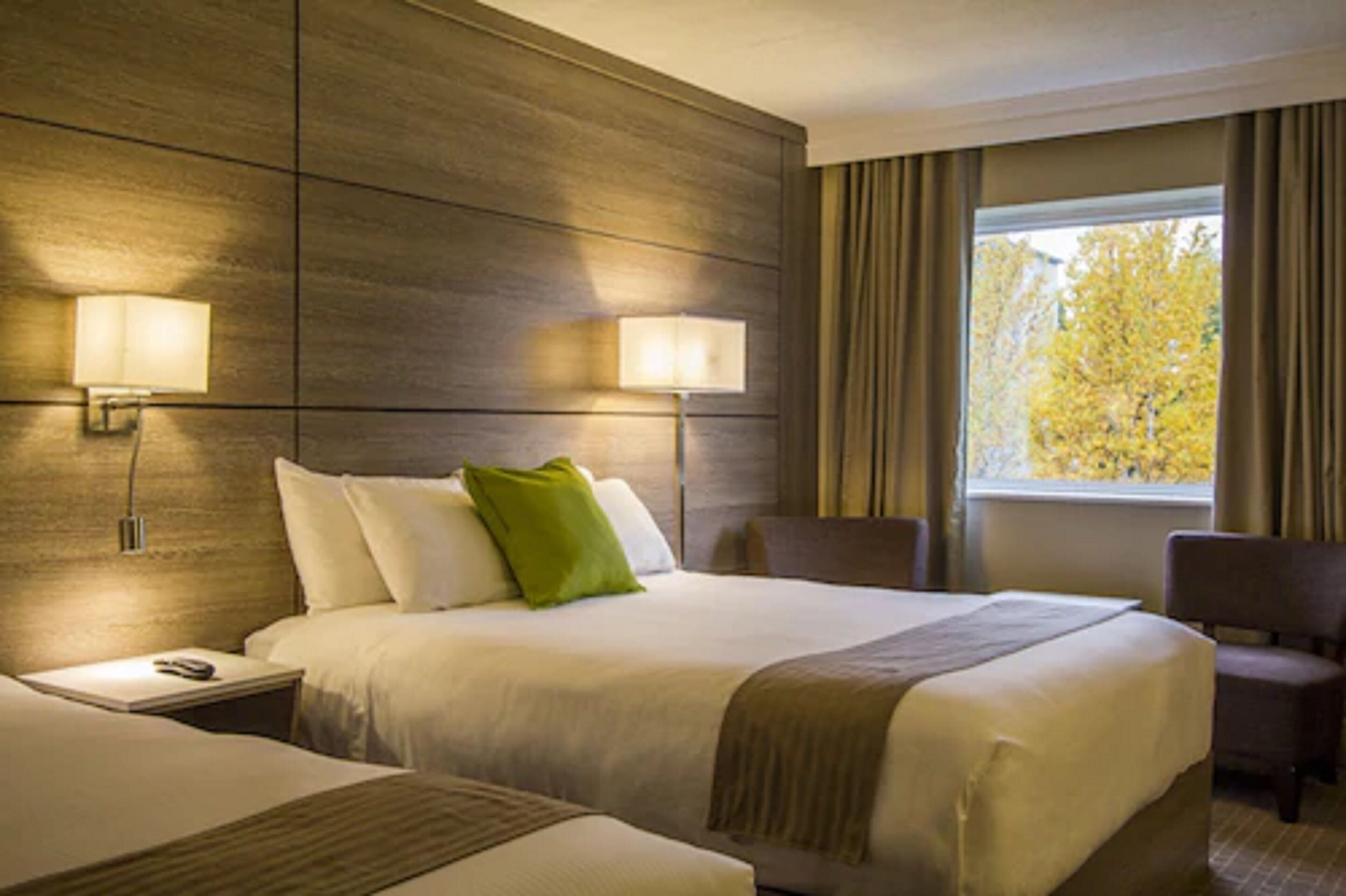 Una habitación de hotel con una cama grande, dos lámparas de noche, una ventana con cortinas y una silla.