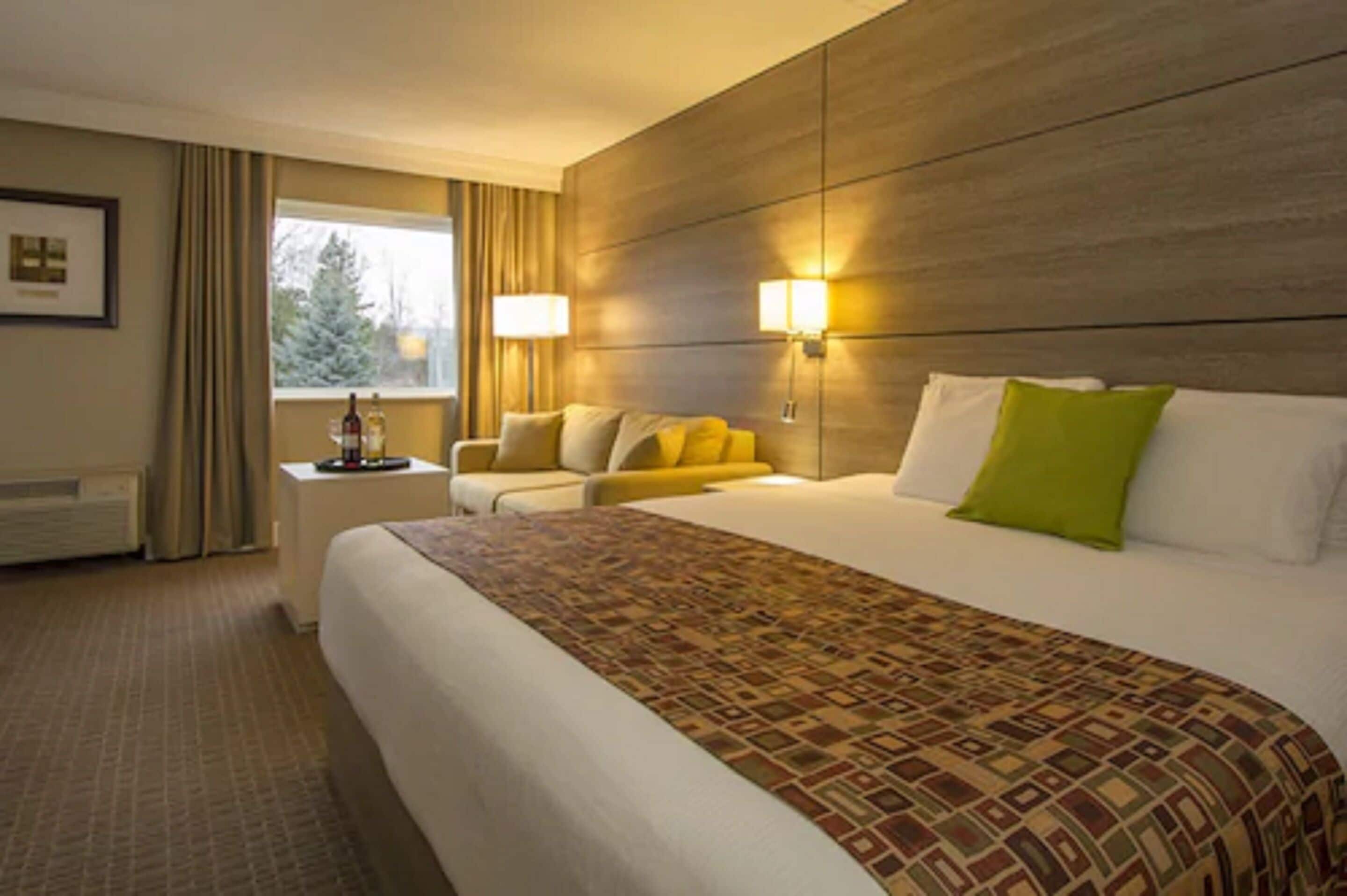 Een hotelkamer met een groot bed, een nachtkastje, een lamp en een raam met gordijnen.