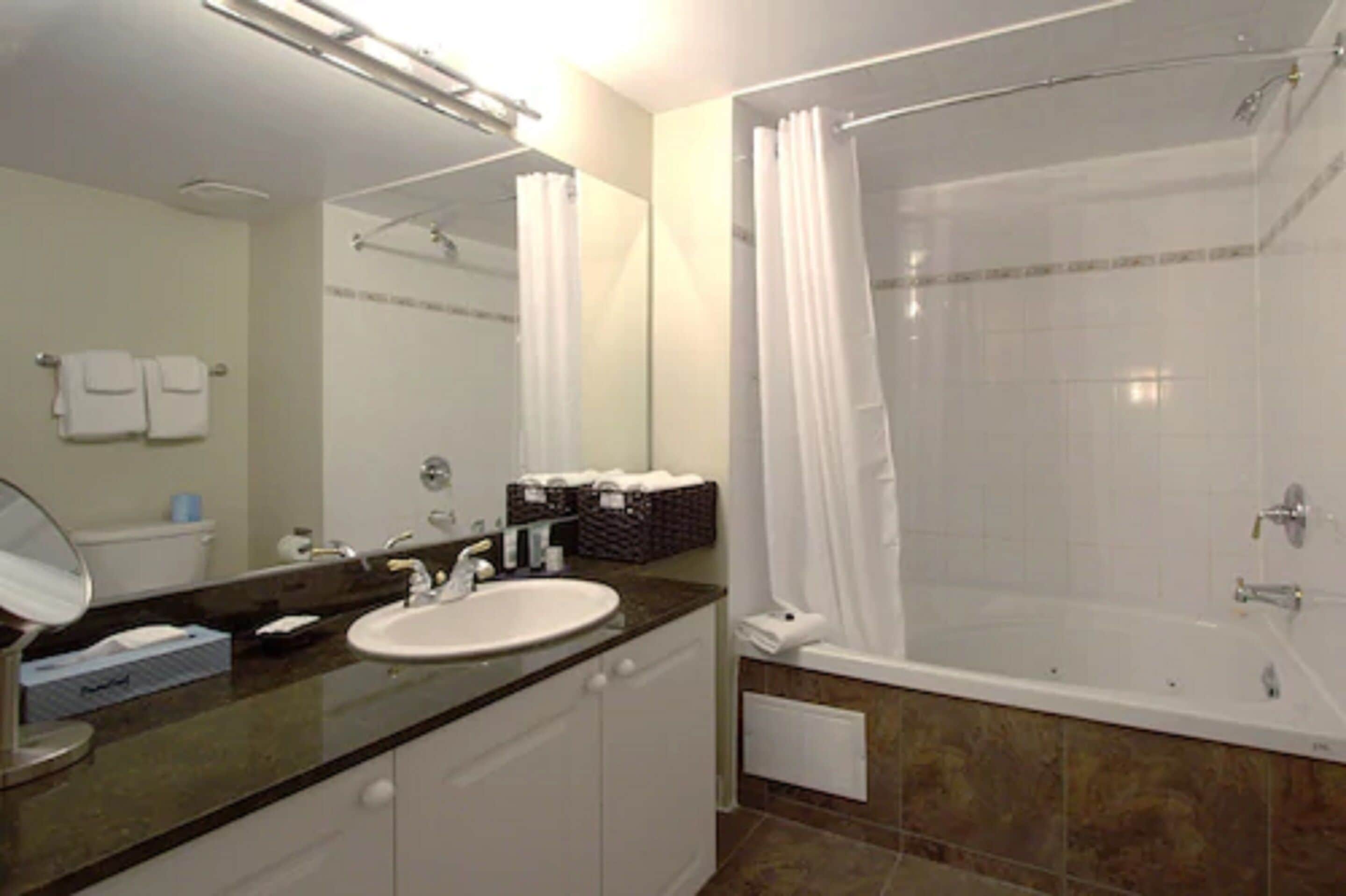 A bathroom with a sink, mirror, and shower area.