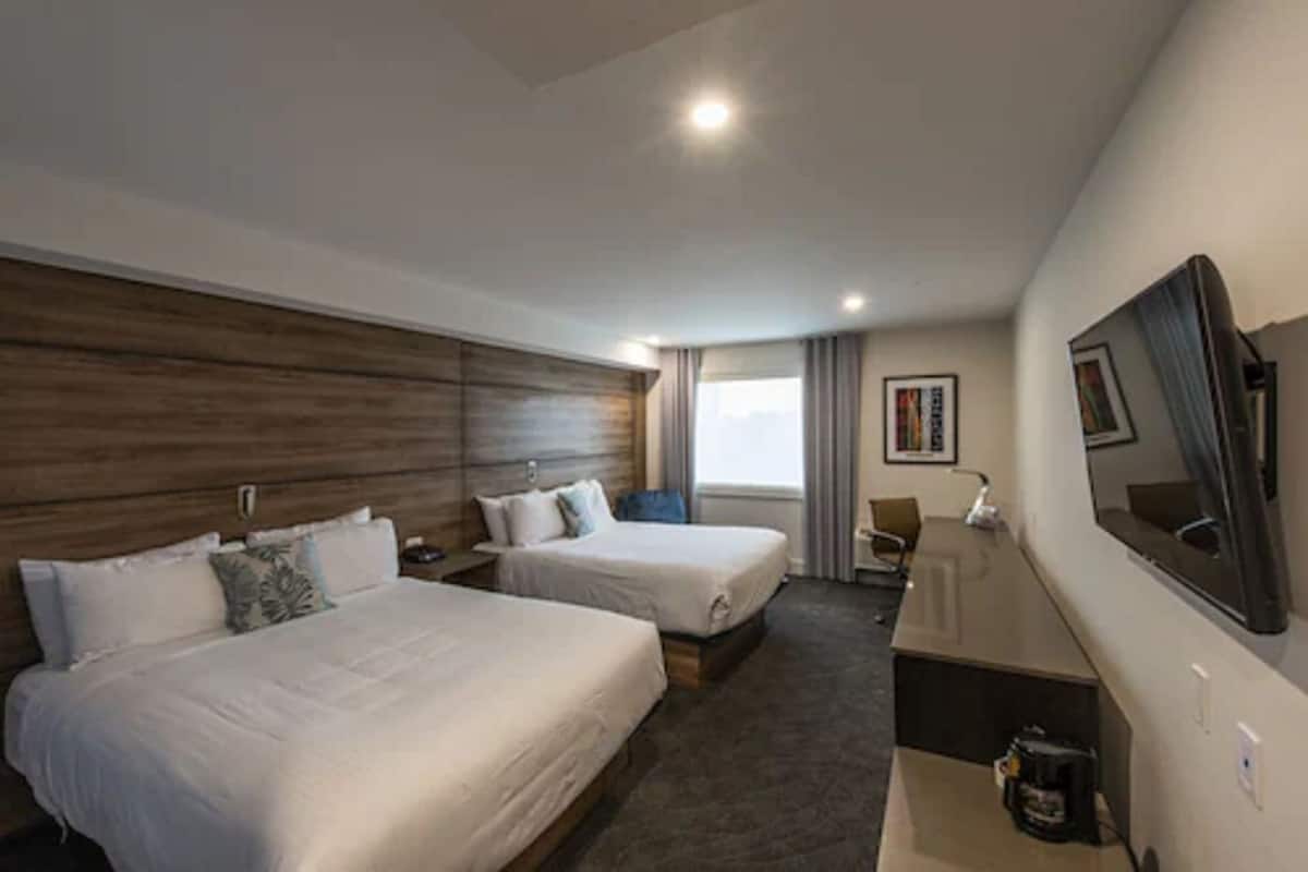 A hotel room with two beds, a desk, a TV, and a window with curtains.