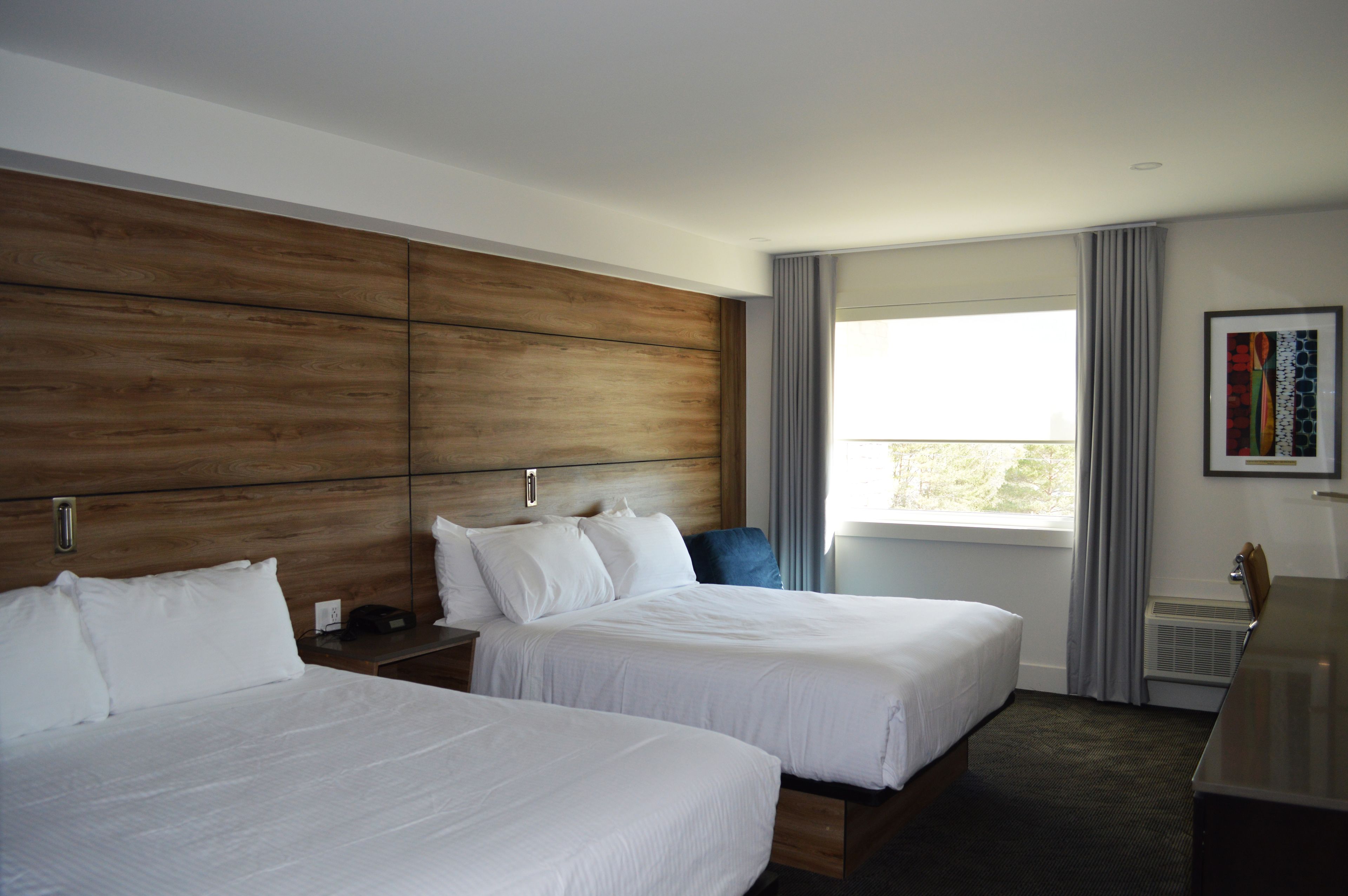 Habitación de hotel con dos camas, cabecero de madera, un ventanal grande con cortinas y un escritorio con silla.