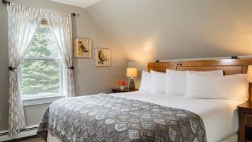 A bedroom with a large bed, a wooden headboard, a nightstand with a lamp, and two wall-mounted bird paintings.
