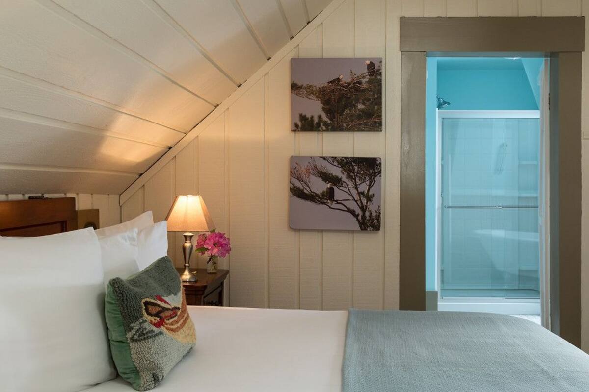 Une chambre à coucher avec un lit, des oreillers, une table de chevet avec une lampe et deux tableaux accrochés au mur.