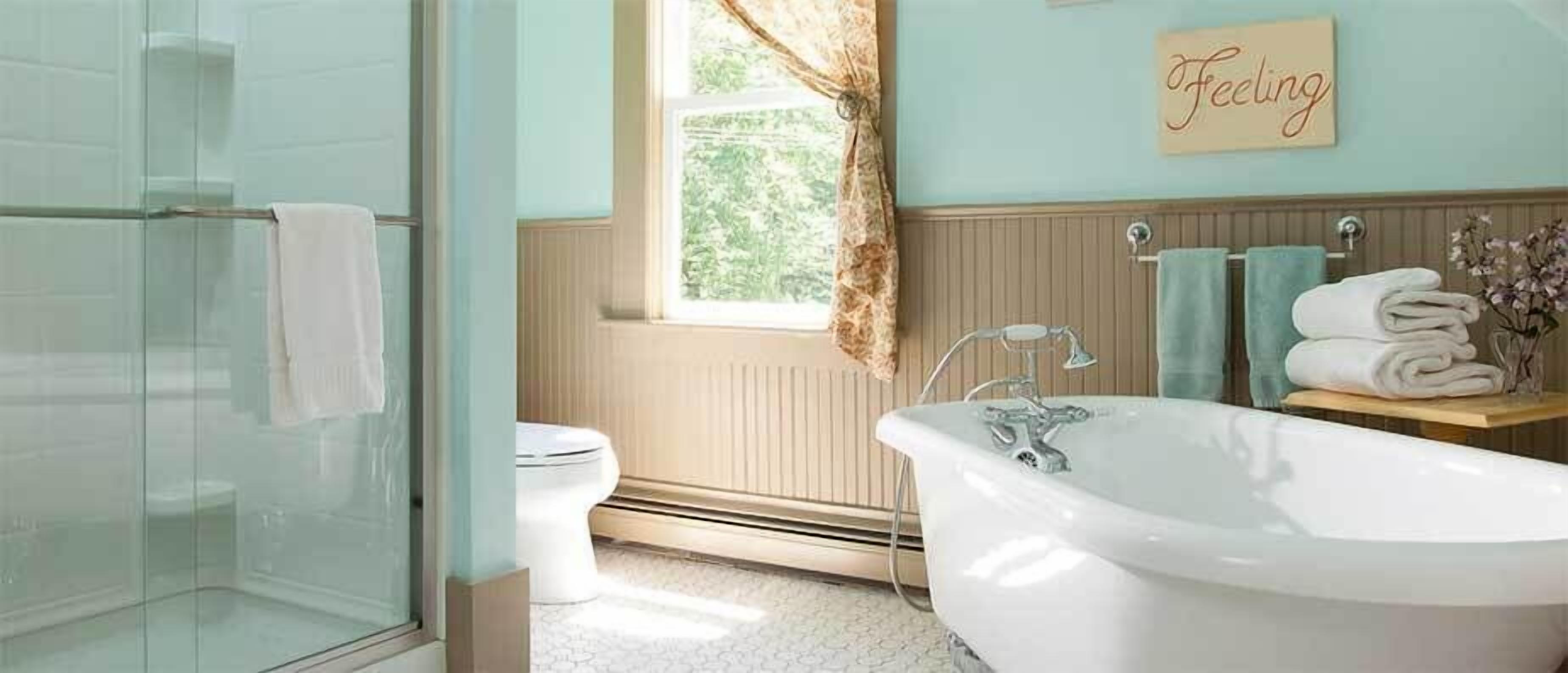 A bathroom with a glass shower enclosure, a white bathtub, a toilet, and a window with a view of greenery.