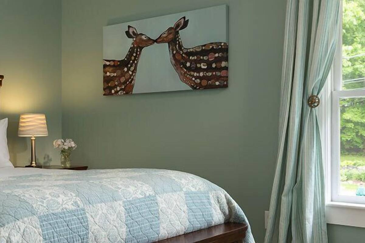 Une chambre à coucher avec un lit, des oreillers, une table de chevet avec une lampe, un tableau décoratif au mur et un tableau.