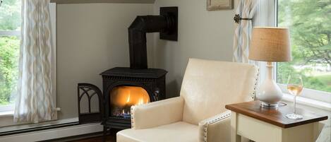 A cozy room with a fireplace, a comfortable armchair, a small table with a lamp, and a window with curtains.