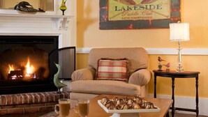 Un salón acogedor con chimenea, un sillón cómodo, una mesita con bebidas y un cartel de Lakeside Paddle Club.
