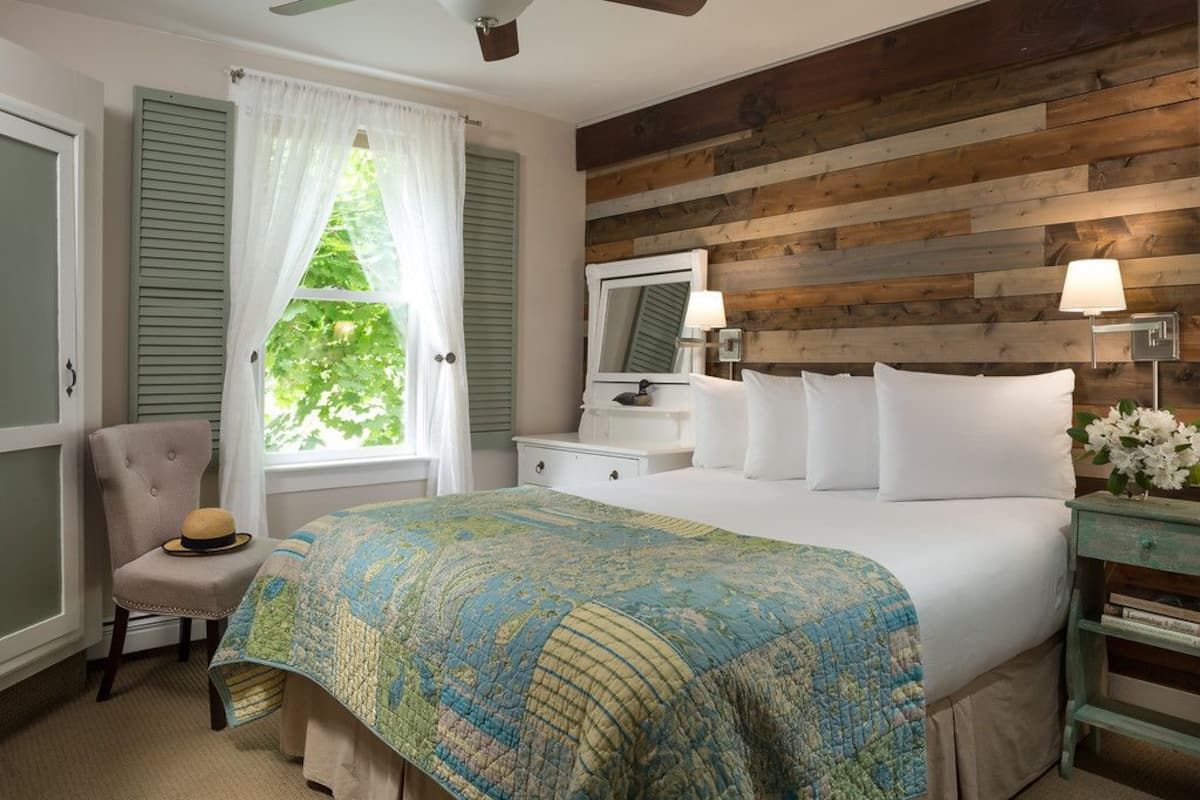 Une chambre à coucher avec un grand lit, une chaise, une table de chevet, un miroir et une fenêtre avec des rideaux.