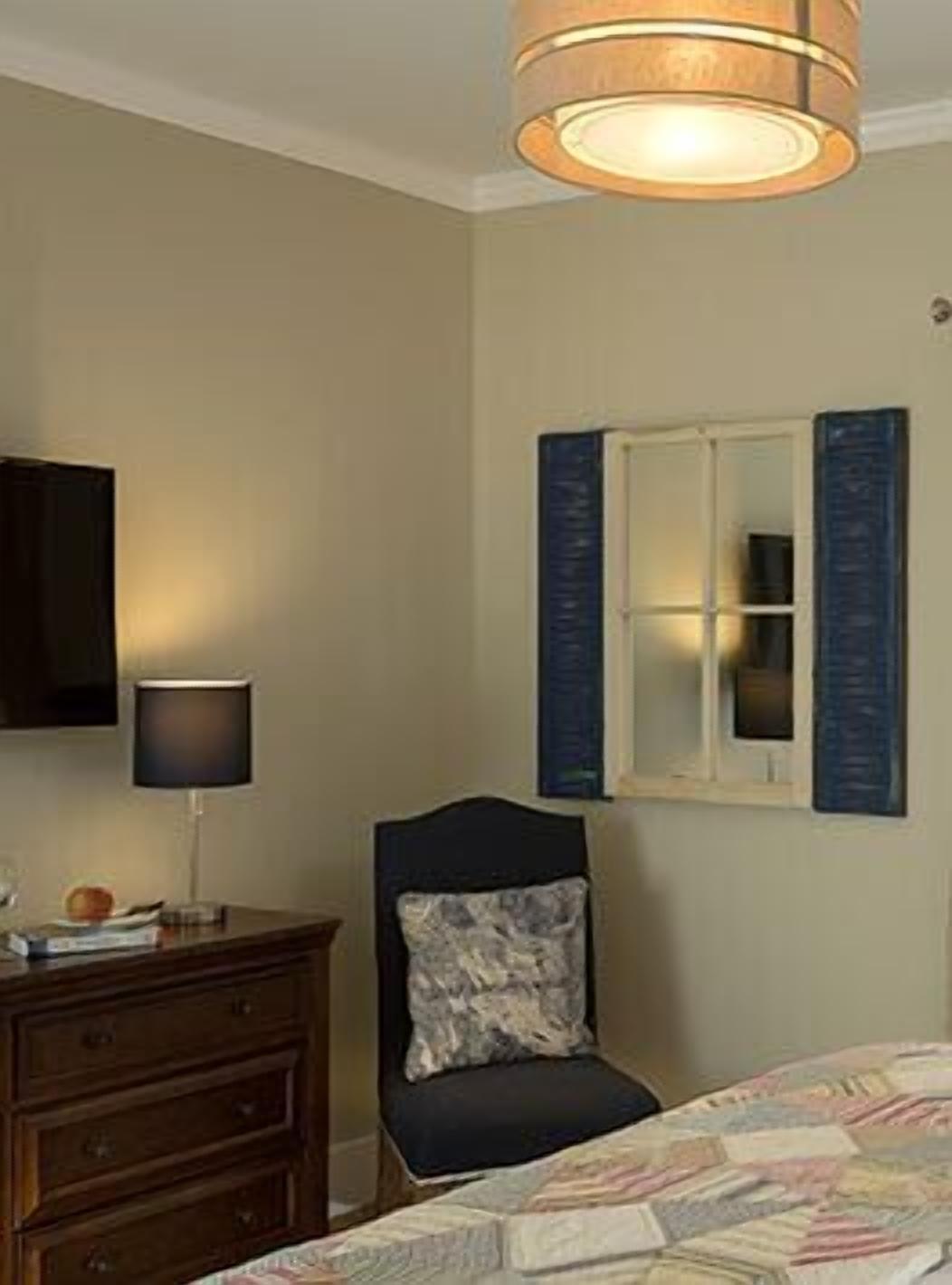 A bedroom with a bed, a dresser, a chair, a lamp, a television, and a window with shutters.