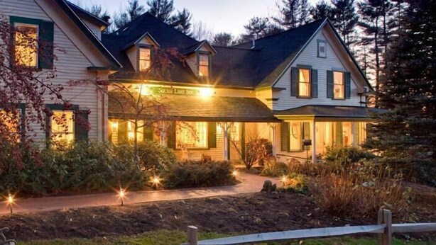 Una casa de dos pisos con un porche, rodeada por un jardín con luces pequeñas.