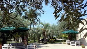 An outdoor seating area with white furniture, green umbrellas, and palm trees. - Cambiocavallo Unesco Area & Resort (Modica)