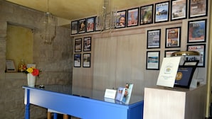 A reception desk with framed travel posters, a vase with flowers, and a clear glass display case. - Cambiocavallo Unesco Area & Resort (Modica)