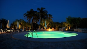 A swimming pool with lounge chairs and umbrellas, surrounded by palm trees and stone walls. - Cambiocavallo Unesco Area & Resort (Modica)