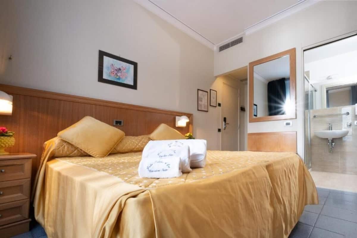 A hotel room with a bed, a nightstand, a framed picture on the wall, and a bathroom visible through an open door.