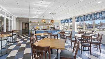 Un restaurant moderne avec un sol à carreaux, des tables et des chaises en bois, un coin bar et de grandes fenêtres donnant sur la rue.