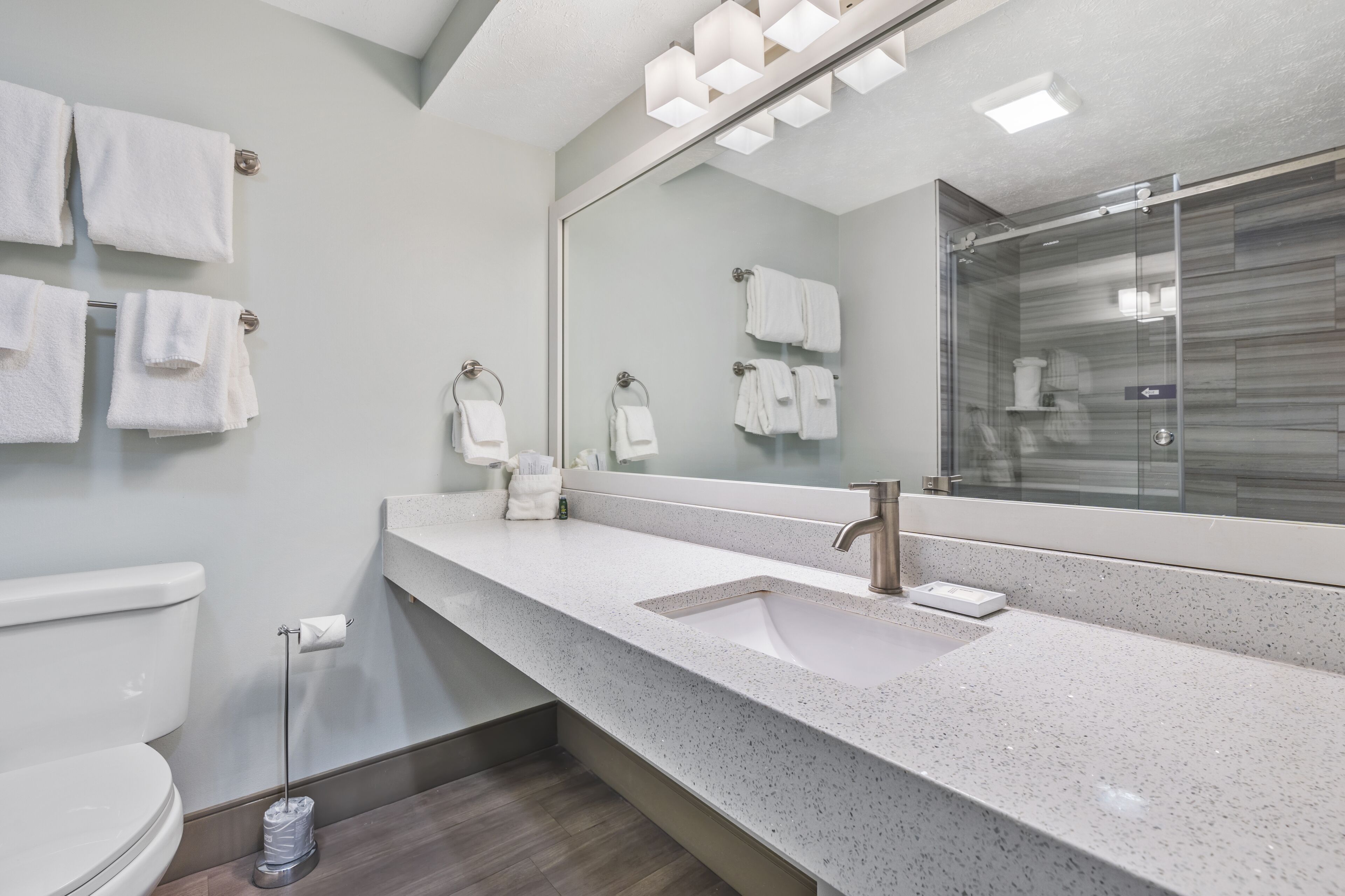 Un bagno moderno con uno specchio grande, un lavandino bianco e diversi ganci per asciugamani.