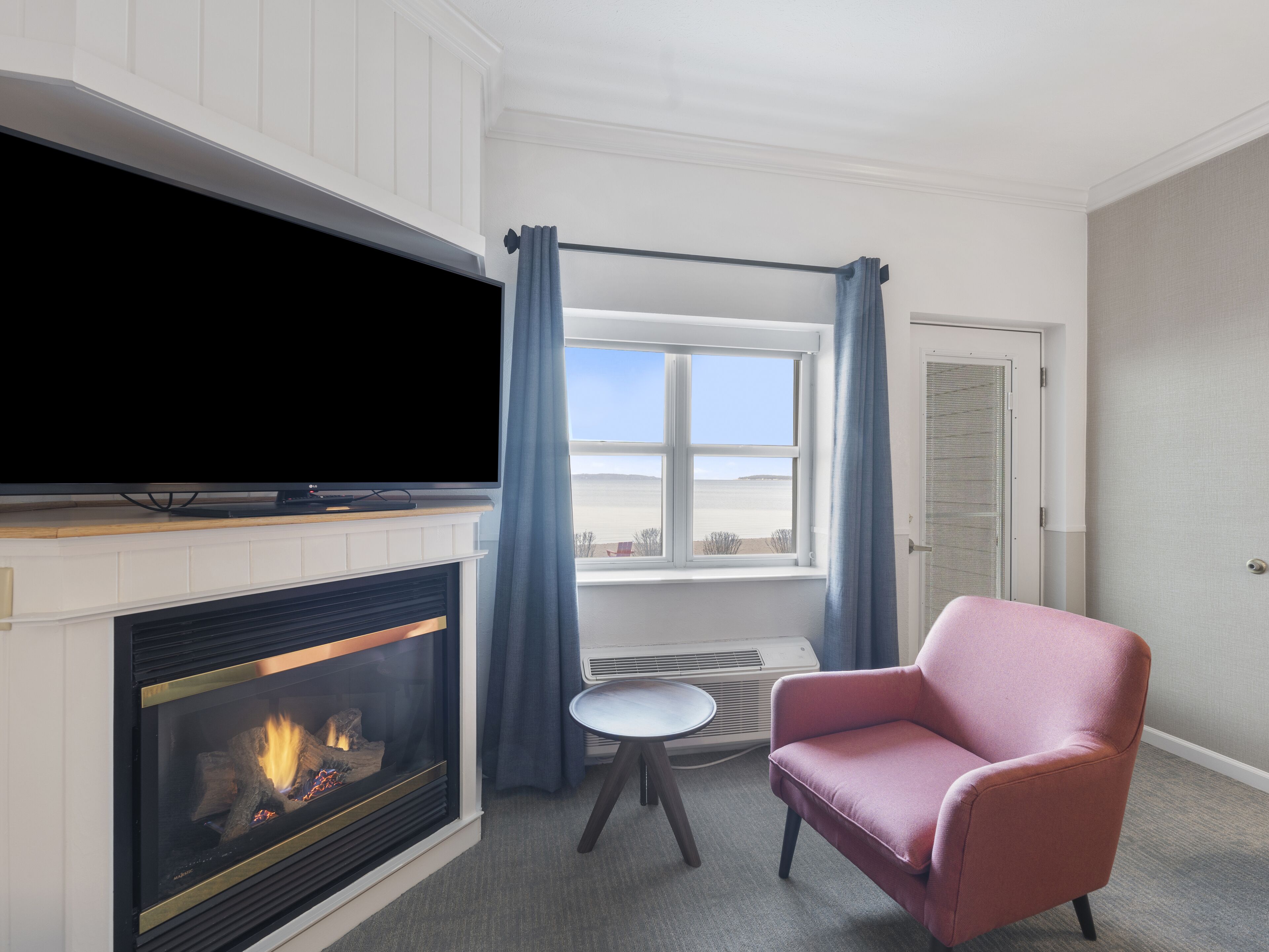 A room with a fireplace, a television, a window with curtains, and a pink chair.