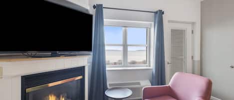 A room with a fireplace, a television, a window with curtains, and a pink chair.