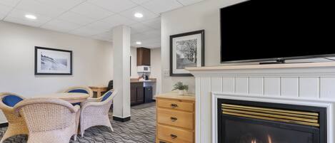 A hotel lobby with a fireplace, a flat-screen TV mounted above it, wicker furniture, and a patterned carpet.