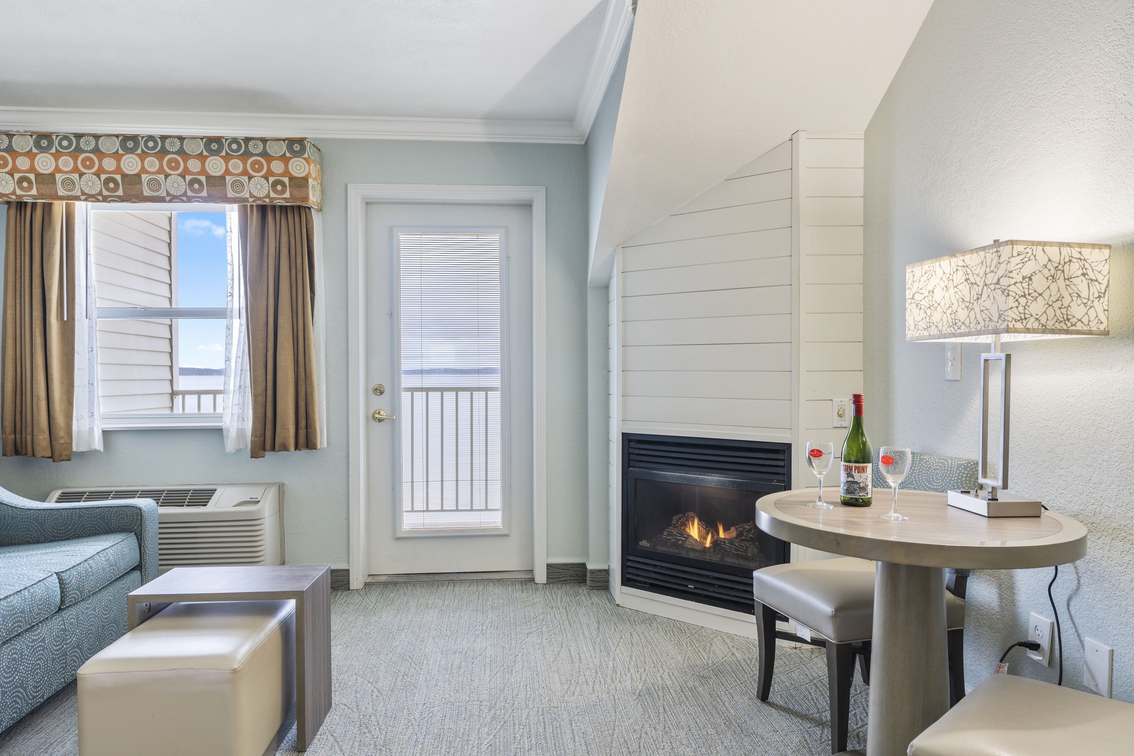 A hotel room with a fireplace, a dining table with two chairs, a sofa, and a small side table.