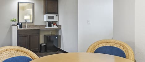 Uma cozinha compacta com micro-ondas, um frigorífico pequeno e uma pia. Há cadeiras de vime ao redor de uma mesa de madeira.
