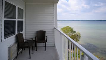 A balcony with two chairs and a table, overlooking a calm body of water and distant land.