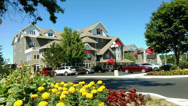 A multi-story hotel with a central entrance, parking lot, and surrounding greenery.