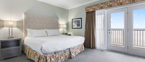 A neatly arranged hotel room with a large bed, a bedside table with a lamp, a framed picture on the wall, and a balcony with curtains.