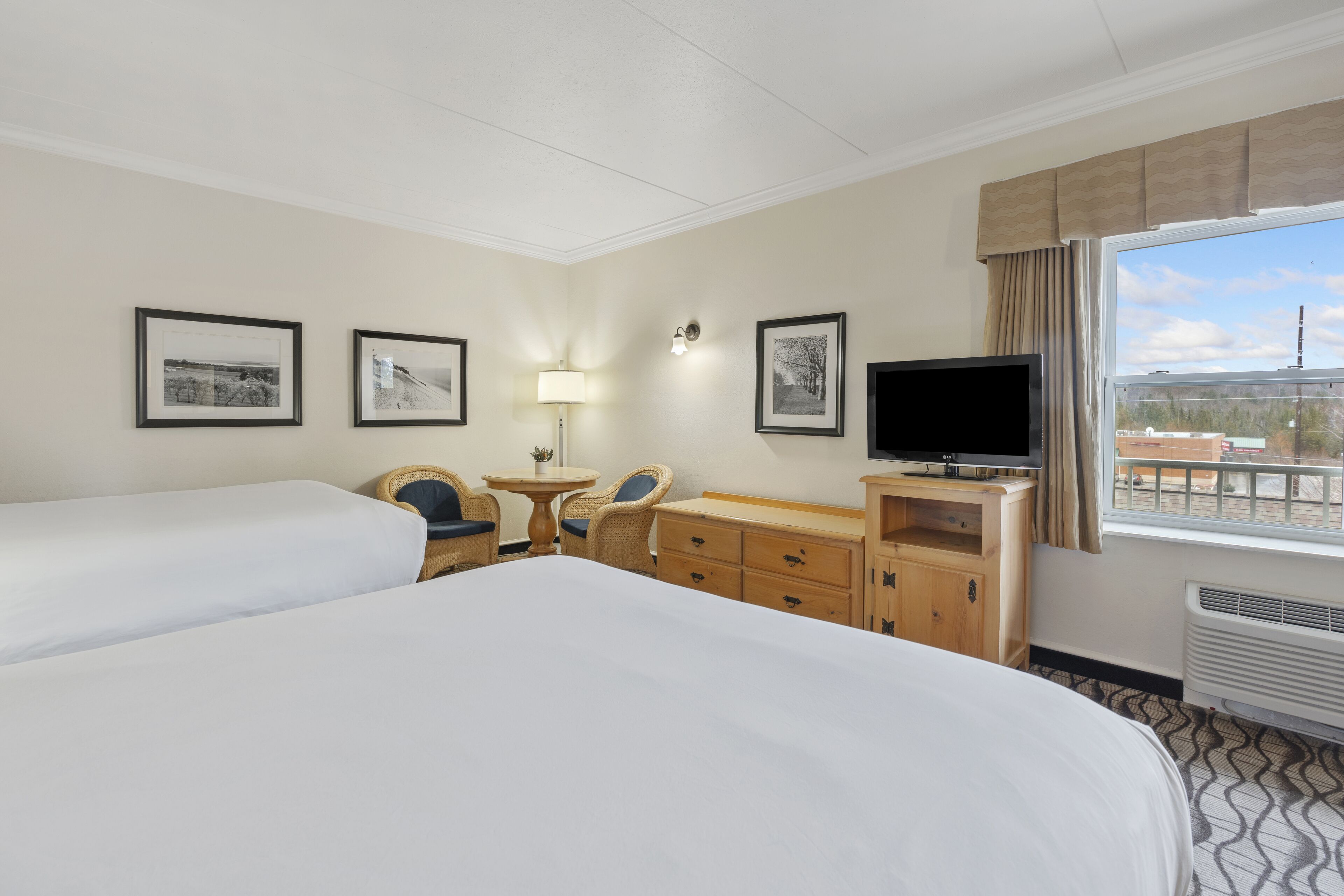 Une chambre d’hôtel avec deux lits, une télévision, un bureau avec une lampe et des tableaux encadrés au mur.