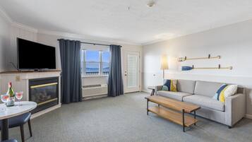 A hotel room with a TV, a sofa, a coffee table, a fireplace, a window with curtains, and a lamp.