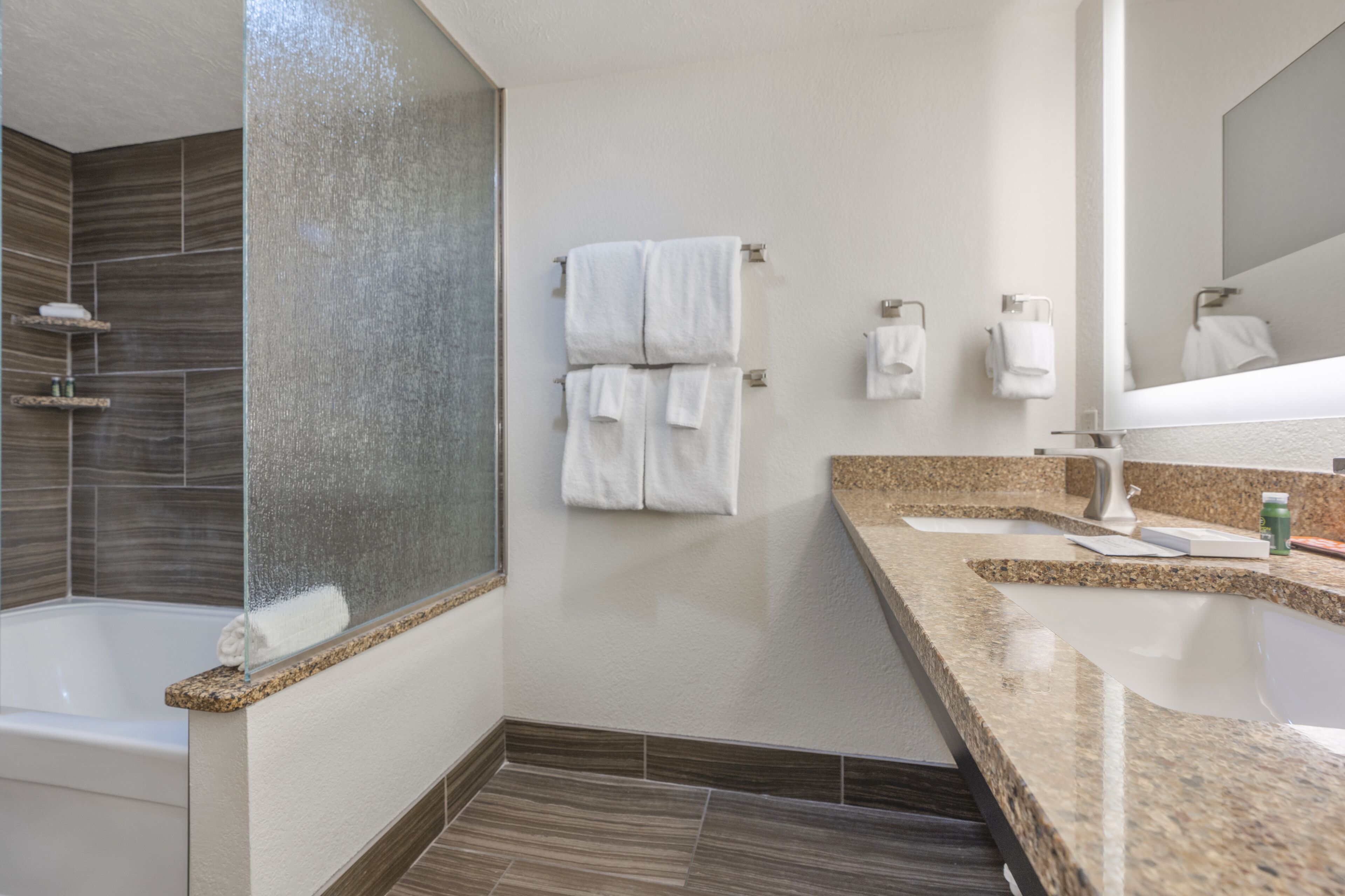 A modern bathroom with a bathtub, a large mirror, and a granite countertop.