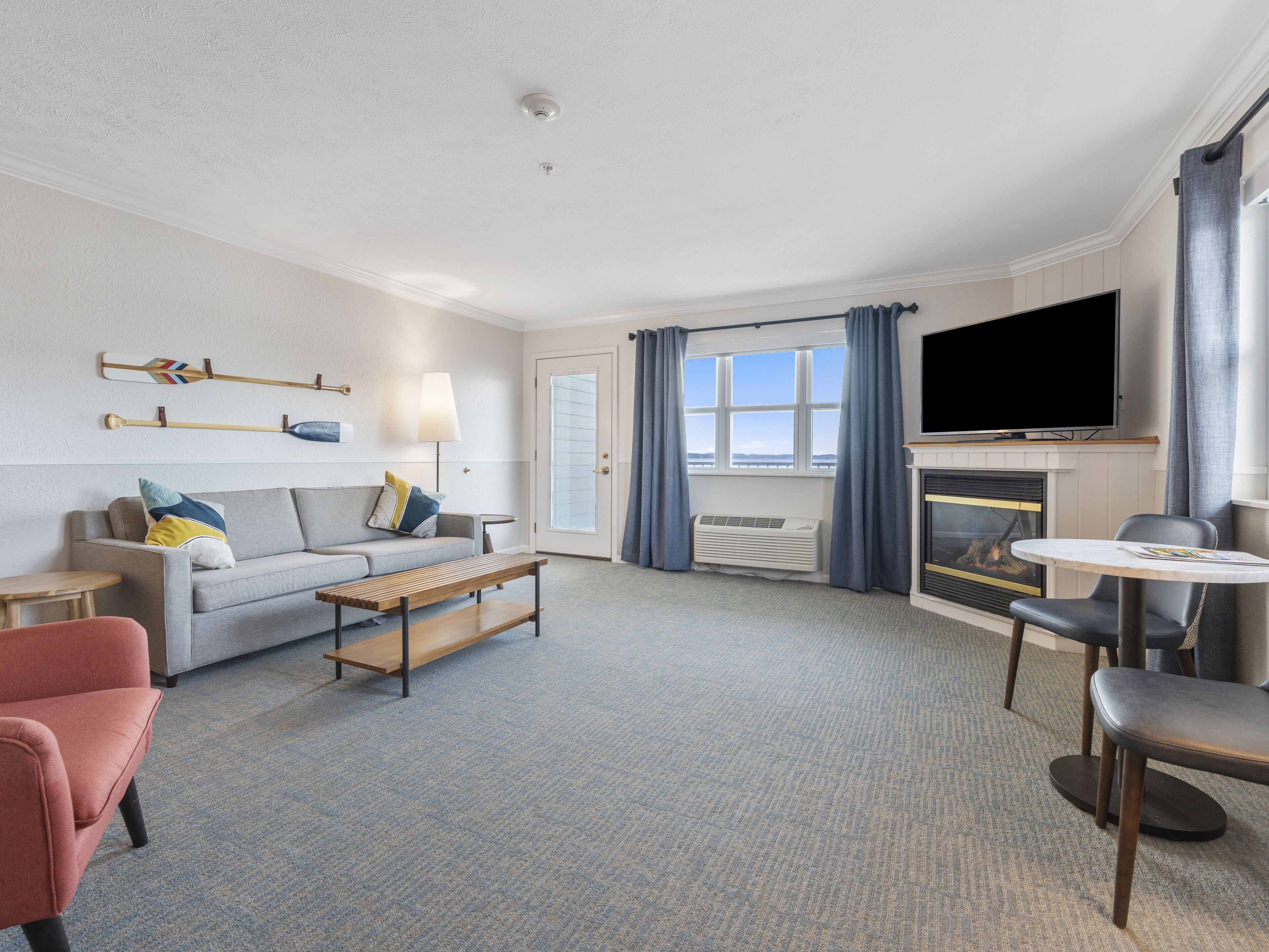Een moderne hotelkamer met een bank, een bijzettafeltje, een houten bankje, een televisie en een open haard.