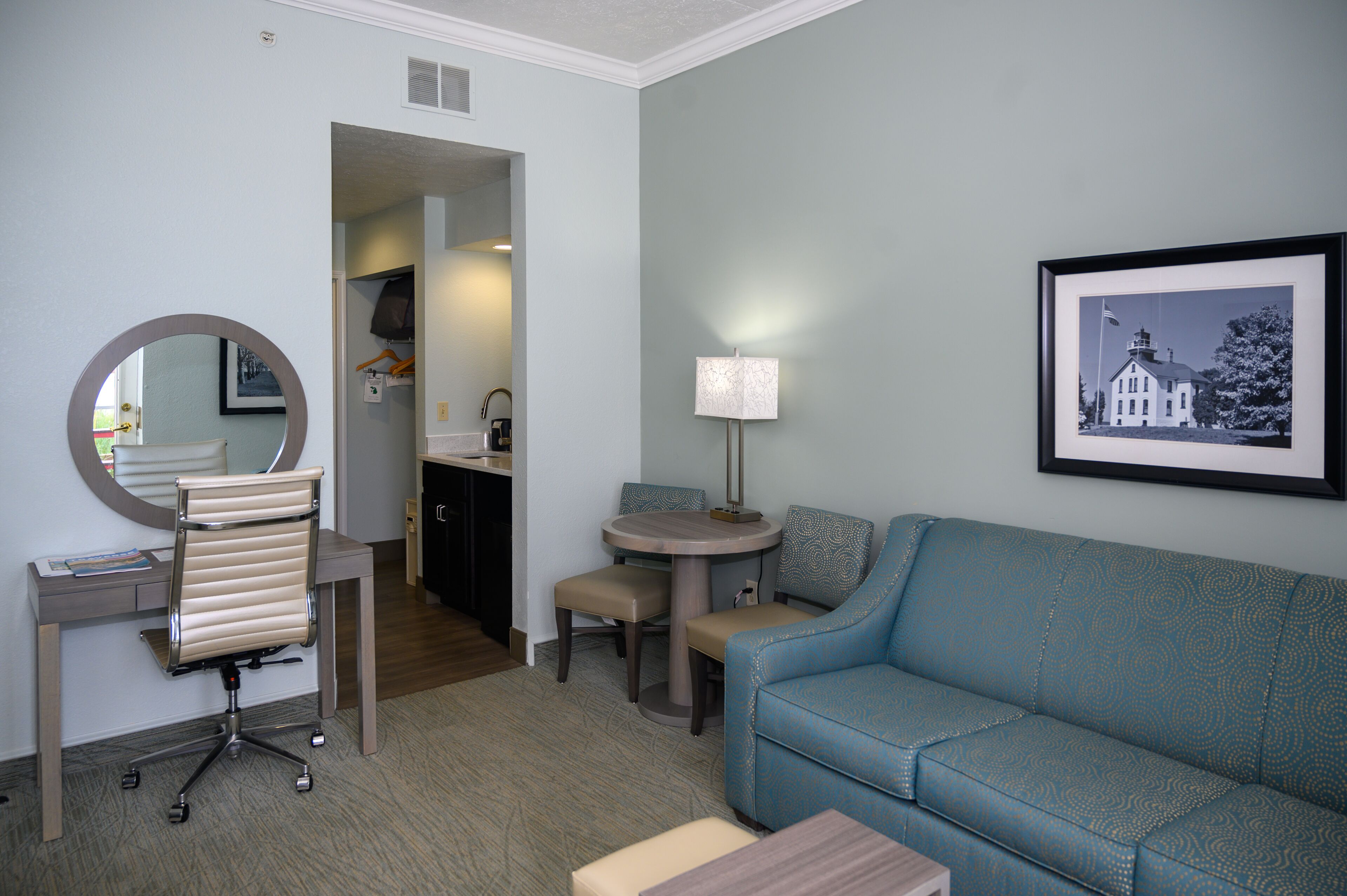 Una habitación de hotel con escritorio, silla, mesa redonda y sofá azul.
