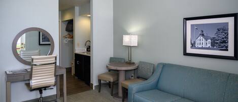 Una habitación de hotel con escritorio, silla, mesa redonda y sofá azul.