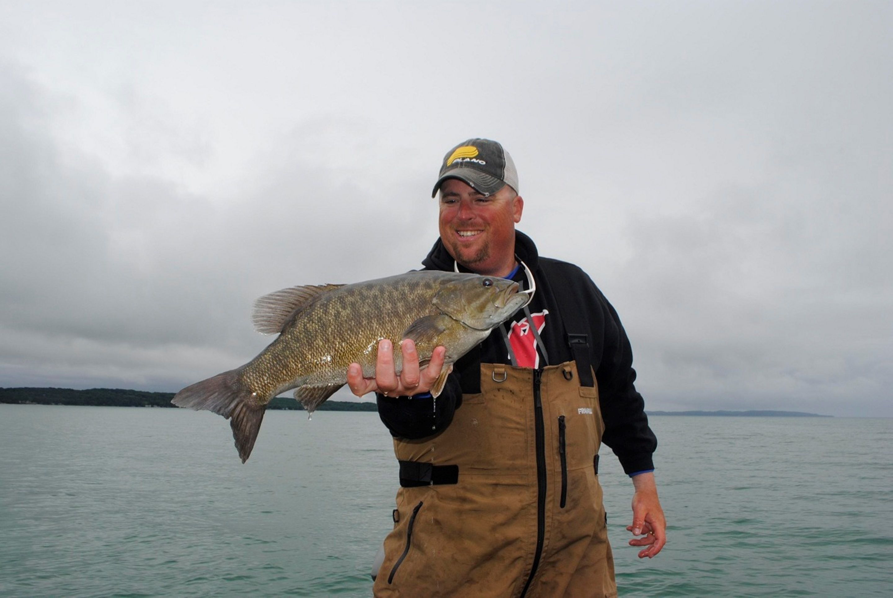 A person holding a fish by a body of water.