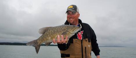 A person holding a fish by a body of water.