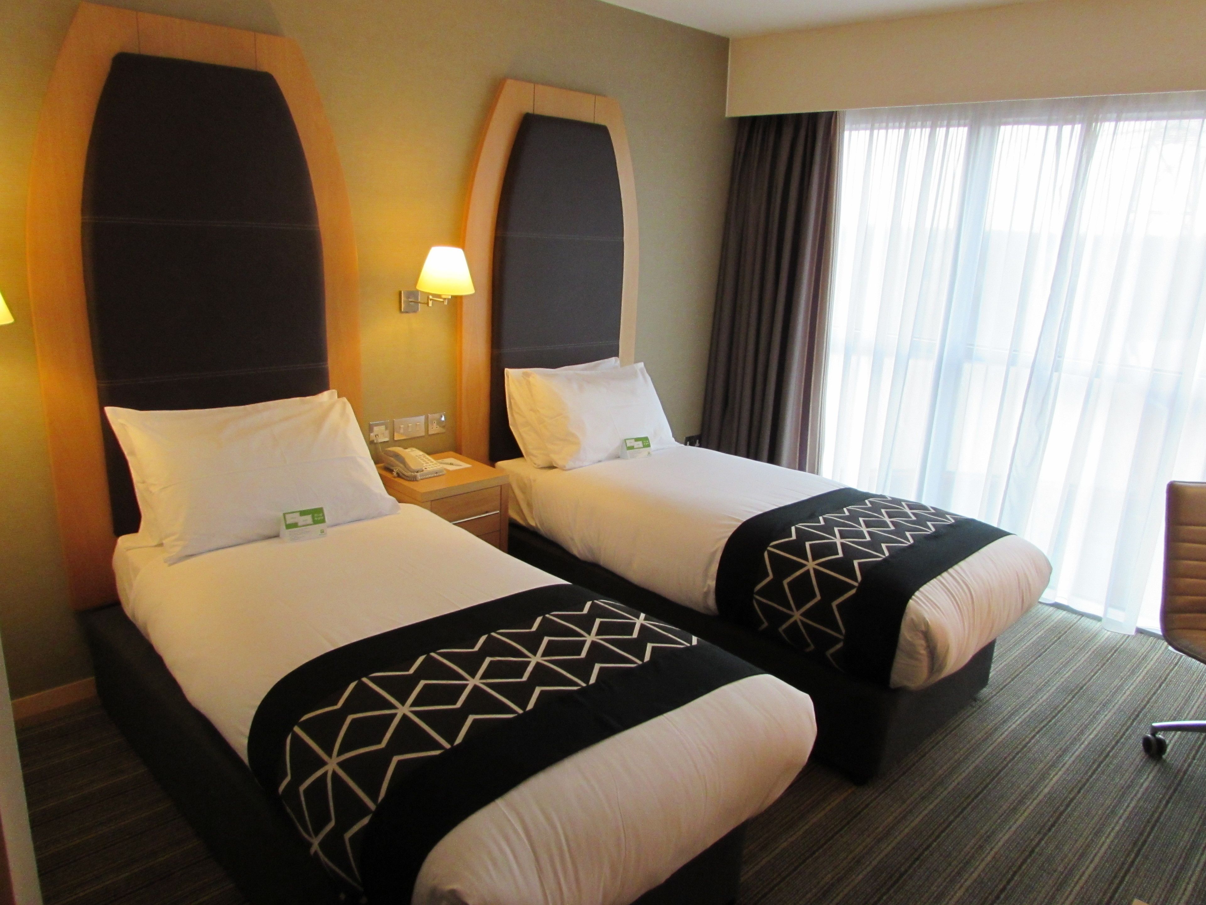 A hotel room with two beds, a nightstand with a telephone, and a window with curtains.