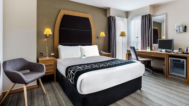 Une chambre d’hôtel avec un grand lit, un bureau avec un ordinateur, une chaise et deux lampes de chevet.