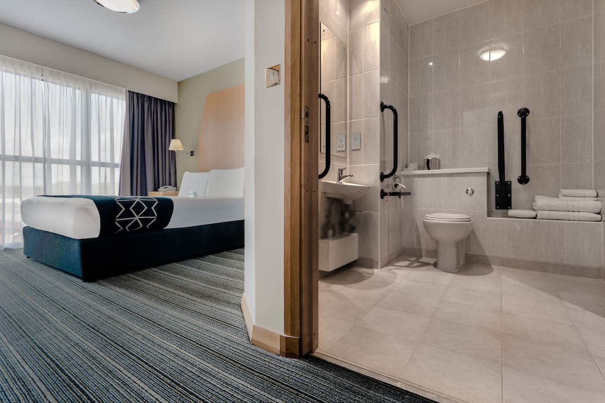 A hotel room with a bed, a bathroom with a toilet, sink, and towel rack.