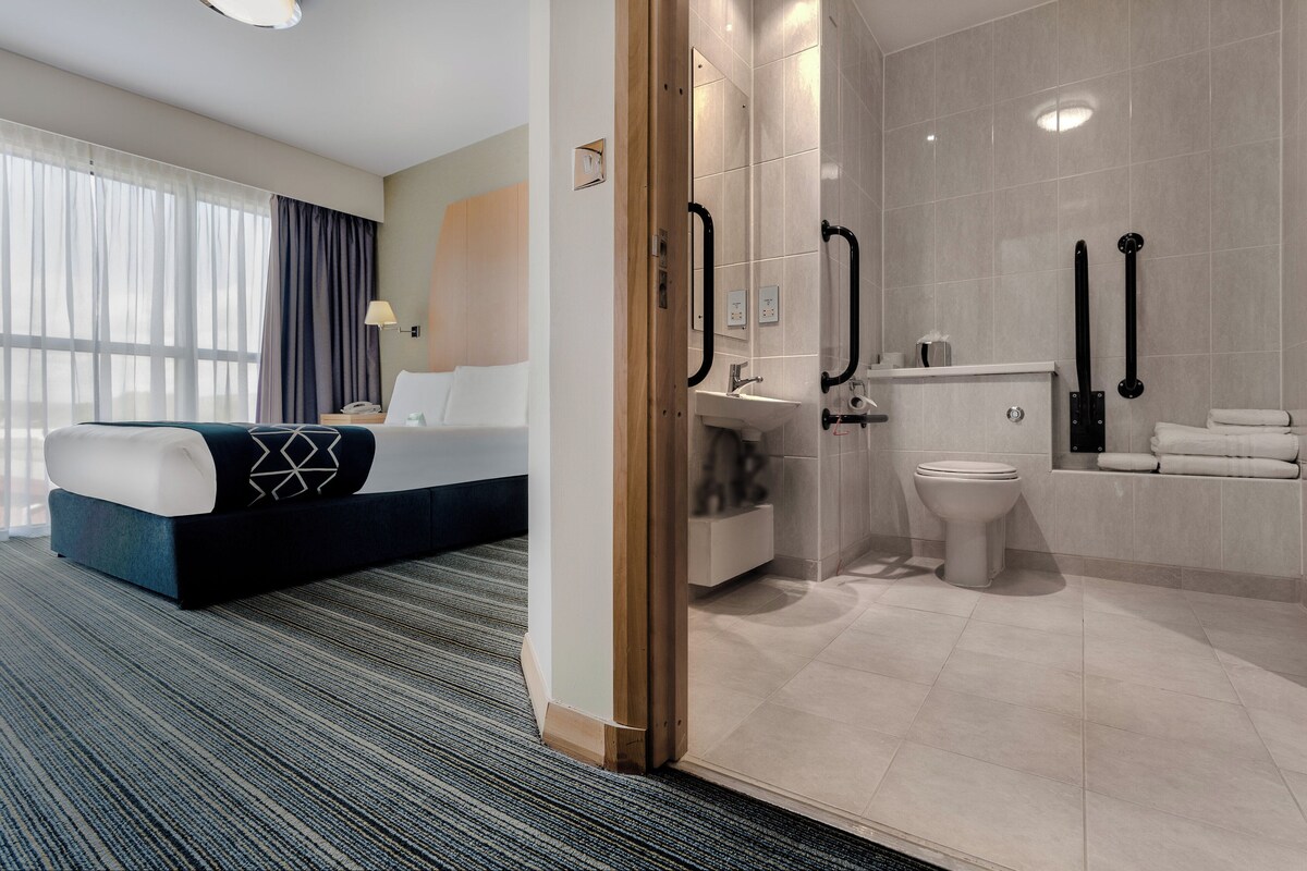 A hotel room with a bed, a bathroom with a toilet and sink, and a shower area.