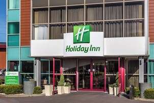 Entrada de un hotel Holiday Inn con señalización clara, puertas automáticas y un cartel de estacionamiento para huéspedes.