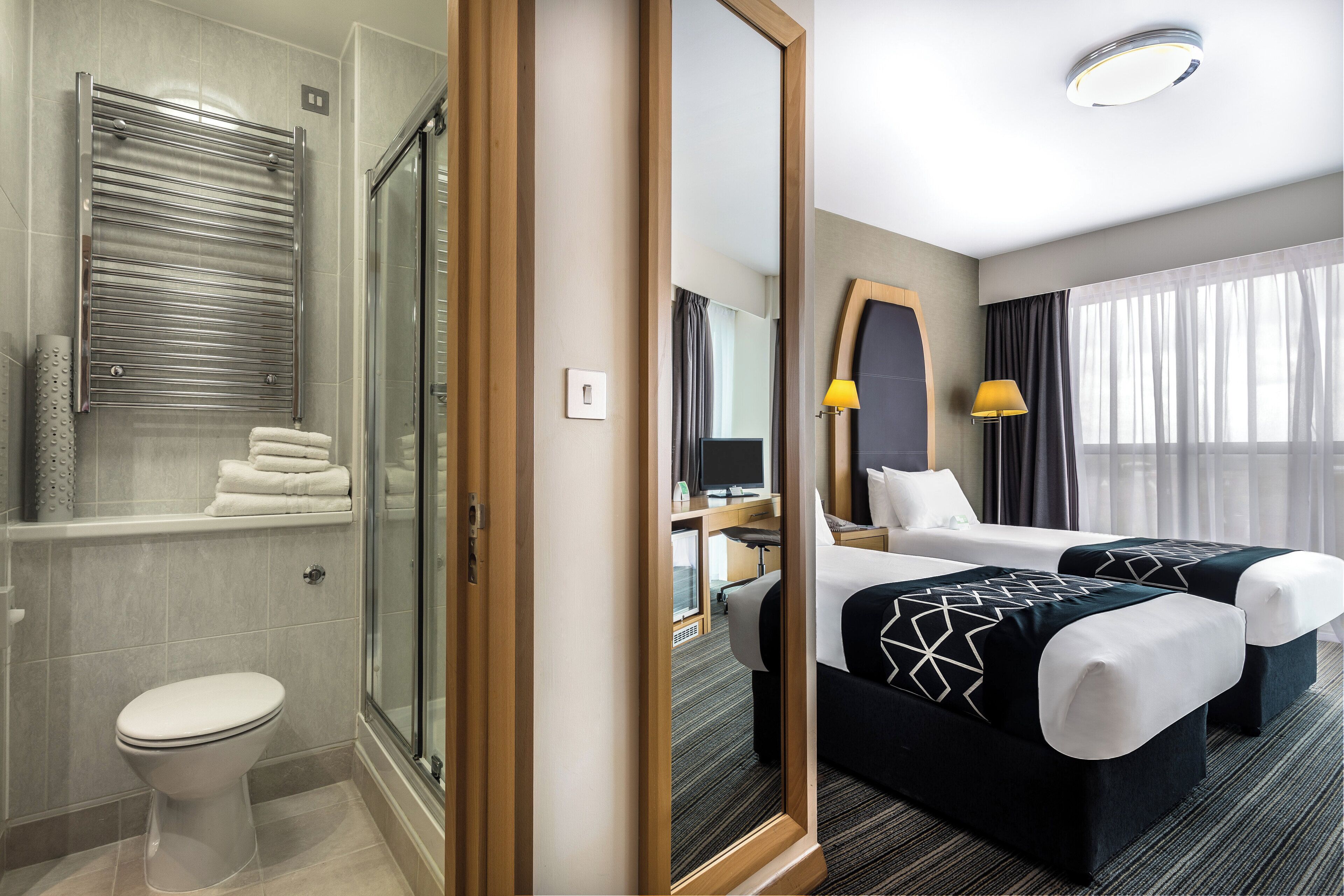 Ein Hotelzimmer mit Dusche, Toilette, zwei Betten, einem Schreibtisch und einem großen Spiegel.